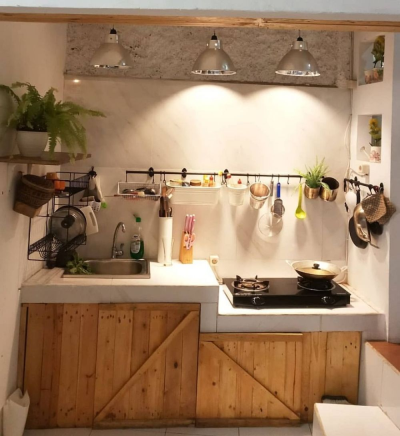 Dapur di bawah ini terlihat sangat sederhana dan minimalis, namun tidak membosankan karena adanya lampu gantung dengan desain menarik berwarna silver dan penutup lemari dapur yang terbuat dari kayu