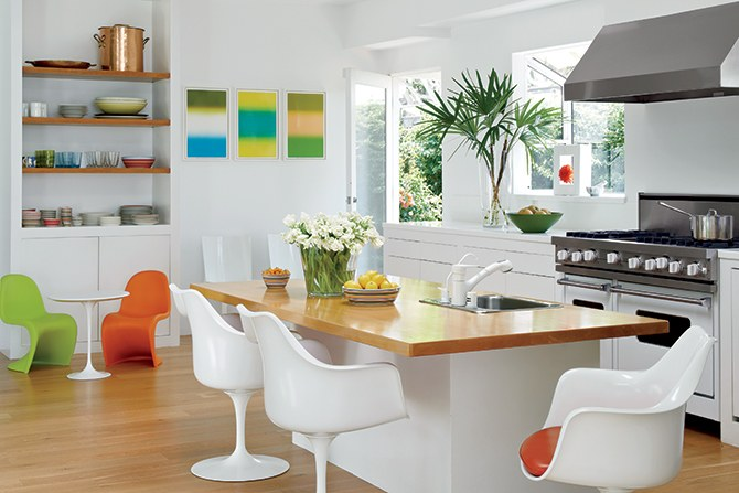 Dapur dengan dominasi warna putih bisa terlihat membosankan tanpa ada sentuhan warna. Cukup berikan hiasan lukisan sederhana dengan warna cerah dan kursi plastik berwarna hijau dan orange untuk tempat bersantai