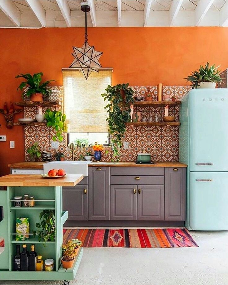 Untuk anda yang tidak takut bermain dengan warna, anda bisa mendesain ulang dapur dengan latar belakang dinding yang berwarna orange. Lalu tambahkan sedikit corak dengan warna senada, tidak lupa semburat warna biru muda pada kulkas dan hijau pada rak dapur