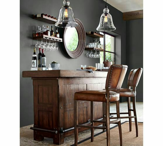 Untuk lebih menciptakan kesan bar seperti bar original pada umumnya, pilih meja bar dengan material kayu dan kursi bar tinggi berwarna cokelat. Tidak ketinggalan rak botol juga lampu gantung